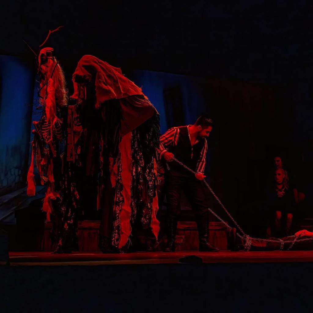 A stage with a Krampus puppet and a person dragging another in chains